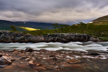 long exposure of a torrent with sun spots on the green hills in the background