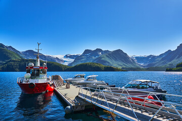 Svartisen glacier and its sourrounding moutains in the background and in the foreground a boat jetty with a big red boat