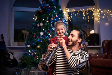 Laughing and happy daughter celebrating a New Year with her father in living room decorated with xmas tree and lights.
