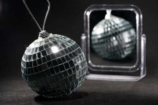 A shiny silver disco ball ornament in front of a mirror