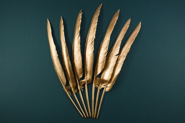 The Golden feather. Pattern with gold colored feathers on a trendy green emerald background. The...