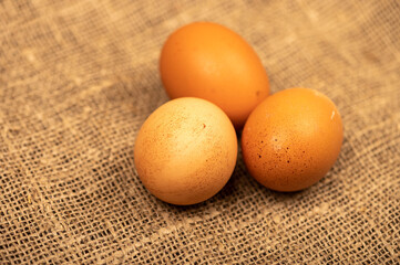 A few yellow, large chicken eggs on a background of homespun fabric with a rough texture. Close-up, selective focus.