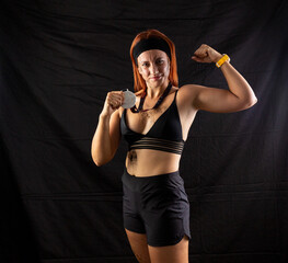 Beautiful redhead girl in sportswear with a silver medal in the studio on a black background