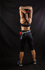 Beautiful girl in a jogging red uniform warming up before training in the studio on a black background