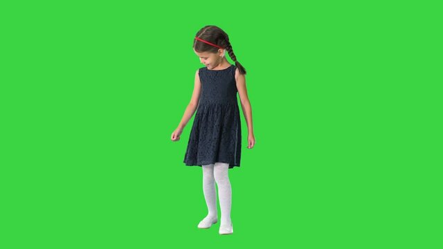 Cute little girl with pigtails in black dress walking looking down at her feet and then smiling at camera on a Green Screen, Chroma Key.