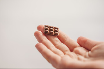 Miniature: a bar of dark chocolate made of polymer clay on the fingertips of a woman's hand.