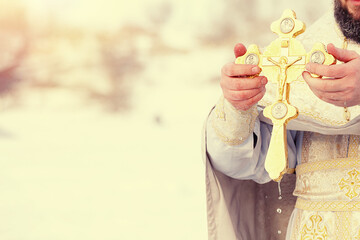The hands of a priest dip an Orthodox gold cross into the river. Feast of the Epiphany of Russia. Toned image.