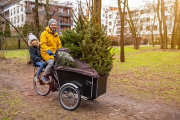 Father and daughter having a ride with cargo bike transporting Christmas tree