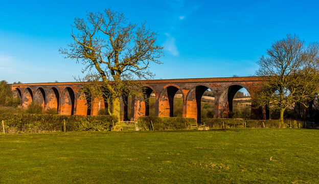 Leafless Winter Trees Against A Backdrop Of The Victorian Railway Viaduct For The London And North Western Railway At John O'Gaunt Valley, Leicestershire, UK In Winter