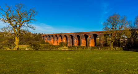 Leafless winter trees frame the Victorian railway viaduct for the London and North Western Railway at John O'Gaunt valley, Leicestershire, UK in winter