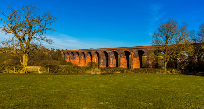 Leafless Winter Trees Frame The Victorian Railway Viaduct For The London And North Western Railway At John O'Gaunt Valley, Leicestershire, UK In Winter