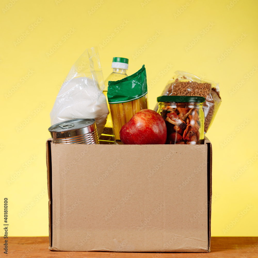 Wall mural Donation Box With food For Donation On Yellow Backround. Assistance To The Elderly In The Context of The Coronavirus Pandemic. square image