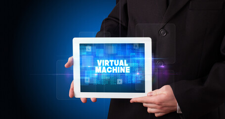 Young business person working on tablet and shows the inscription: VIRTUAL MACHINE