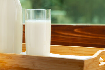 Bottle and glass of milk on wooden table against blurred foliage background