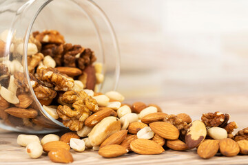 A mixture of different nuts is poured from a glass jar onto the table. Nuts as texture and background, macro
