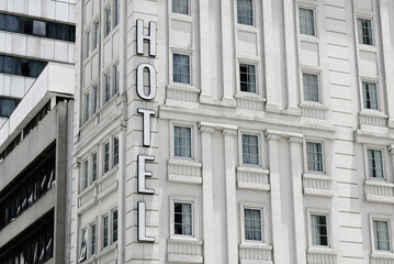Outdoor view of Hotel sign of building with windows with curtain on white wall.