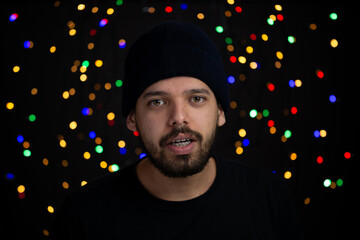 Young man frontal portrait in a studio shot with holiday lights in the background.