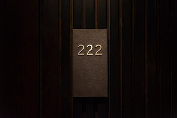 Hotel room with 222 number, dark wood door, black number plate with golder numbers