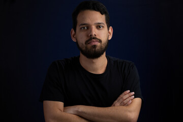Frontal portrait of young men serious with arms crossed. He is over a black background.