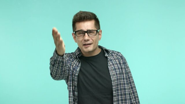 Frustrated and disappointed brunette man in glasses staring at something upsetting, shaking head and pointing at camera angry, standing over turquoise background