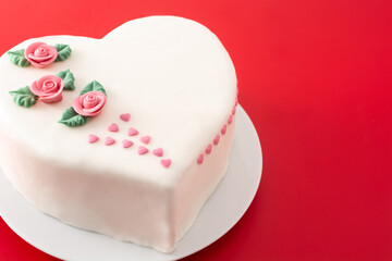 Fototapeta na wymiar Heart cake for St. Valentine's Day, Mother's Day, or Birthday, decorated with roses and pink sugar hearts on red background 
