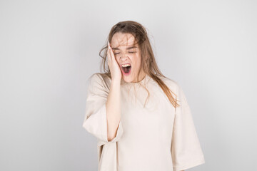 A picture of a sleepy, attractive Caucasian woman with disheveled brown hair, feeling tired after a night without sleep, yawning, covering her open mouth with her hand