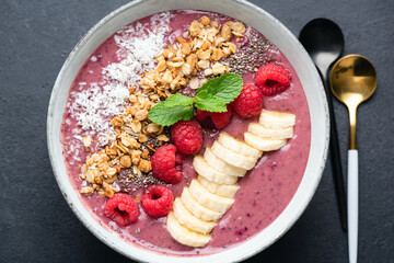 Healthy vegan fruit smoothie bowl with toppings crunchy oat granola, raspberries, banana slices and shredded coconut. Top view