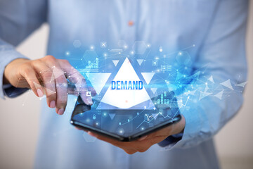 Businessman holding a foldable smartphone with DEMAND inscription, business concept
