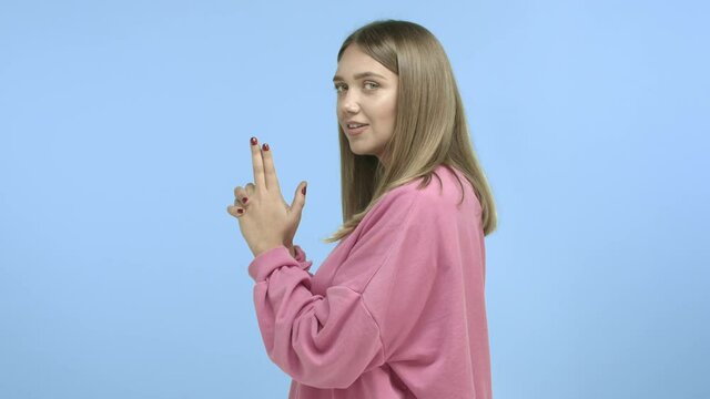 Slow-motion of attractive young woman standing in profile with gun gesture, acting like secret agent or spy, turn head at camera and nod with smug face, blue background