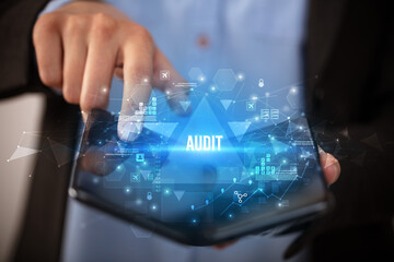 Businessman holding a foldable smartphone with AUDIT inscription, business concept