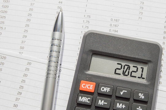 2021 is written on the calculator display, on the desktop with financial documents and a pen. Business concept