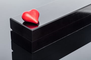 red shape volumetric heart lies on a black gift box on black glass with reflection, background on the theme of celebrating valentine's day.