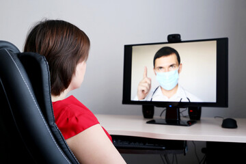 Online consultation with a doctor, woman listens to the physician recommendations sitting in front of the PC webcam. Man in medical mask on the monitor during video chat