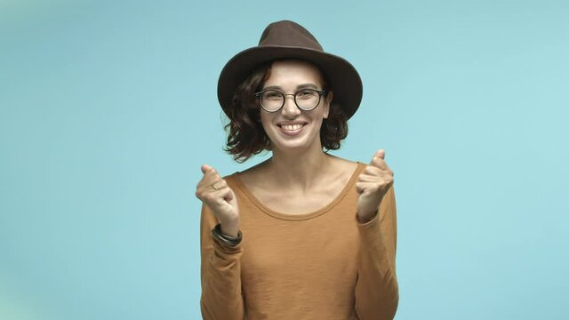 Happy young woman rejoicing, smiling and screaming yes with joy, winning prize and celebrating, standing in glasses and fancy hat over blue background