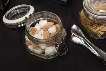 Glass bowl with white and brown lump sugar and forceps on the table for tea and coffee, hotel breakfast