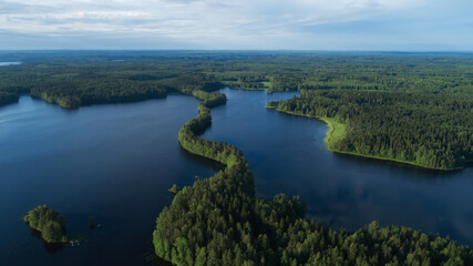 Panoramic aerial view of a lake among the forests. Landscape with drone. Blue lakes, islands and green forests from above on a summer morning. Lake landscape in Finland.
