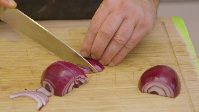 The basic ingredient of almost every good dish is definitely red onion. This is a shot of a chef slicing red onions on a kitchen board.