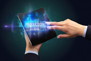 Obraz premium Businessman holding a foldable smartphone with PRODUCTION inscription, new technology concept