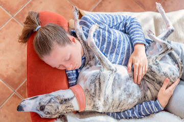 ein junges Mädchen und ihr Whippet Hund kuscheln zu Hause auf dem roten Sofa 