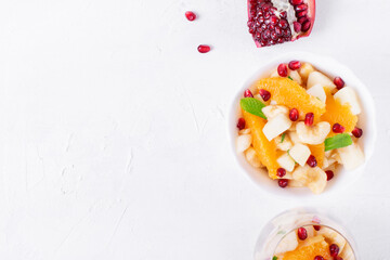 Fruit salad with apple, pear, banana, orange, pomegranate seeds and mint on the white table. Sugar free dessert. Top view. Copy space