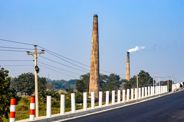 Beside the highway two old brick factories chimney with flying smokes and an electricity pole with wire