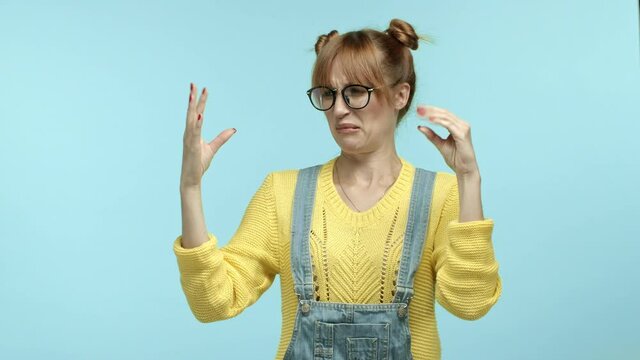 Annoyed hipster woman in glasses and overalls, mocking someone talking too much, showing blah blah blah gesture, making fun of people conversation, standing over blue background