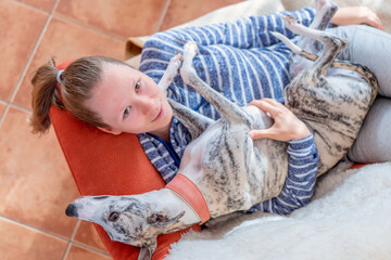 ein junges Mädchen und ihr Whippet Hund kuscheln zu Hause auf dem roten Sofa 