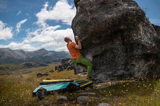 a man bouldering in an orange t-shirt and green pants