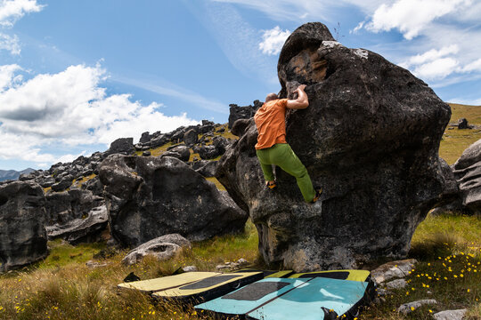 a man bouldering in an orange t-shirt and green pants