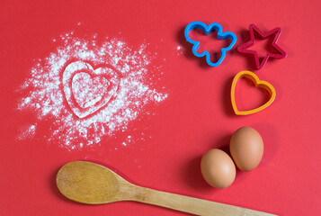 Bakery products. Flour is scattered on the table in the form of hearts. Form for gingerbread. Valentine's day baked goods flour scattered in the shape of a heart on a red background. Christmas 