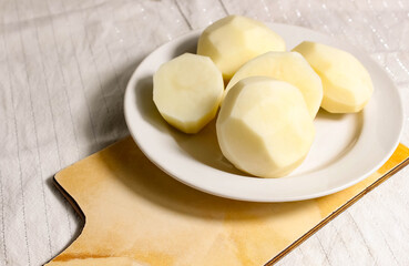 Raw peeled potatoes on a plate and cutting Board.