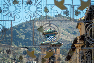 A walk in Granada: Bell tower of the church of Santa Ana seen through a luminous Christmas ornament in the street