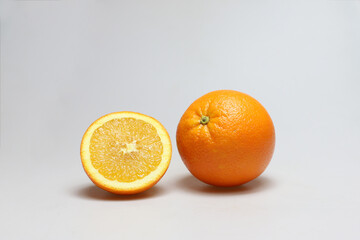 One whole and one half freestanding orange fruits next to each other on a white background