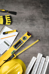 Contractor concept. Tool kit of the contractor: yellow hardhat, libella, hand saw. Plans and notebook on the gray tiles background.
